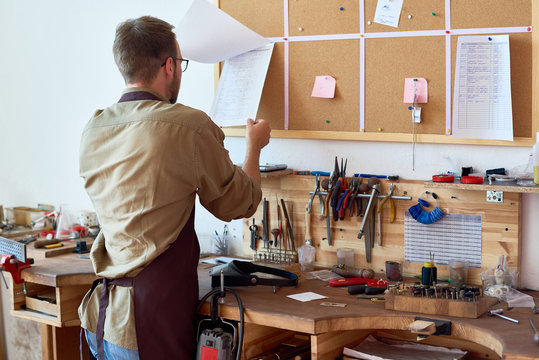 Portrait of man in apron checking order documentation  at workshop table