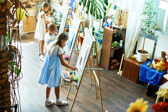 Talented children enjoying painting class at modern art studio, they standing at easels and using watercolor and gouache