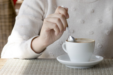 Closeup photo of a woman drinking coffee from a white porcelain cup and a saucer