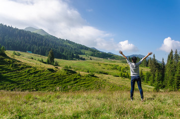 Landscape, travel, tourism. The girl stands on the background of the mountains with her arms outstretched. Horizontal frame