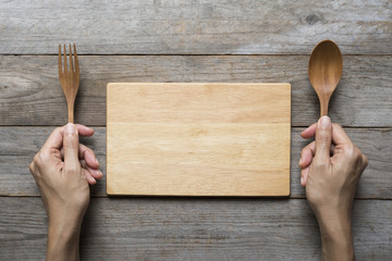 woman two hands hold a spoon and fork and wood dish on table background