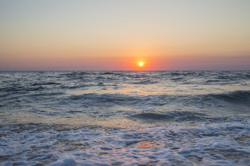 Fototapeta na wymiar Il sole che tramonta nel mare è sempre una bella chiusura per una giornata di vacanza. Le tonalità calde donate dal sole si scontrano con il blu delle acque agitate del mare.