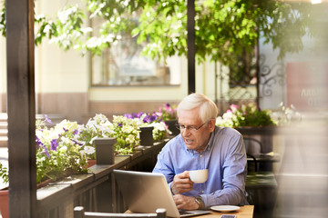 Fototapeta premium Portrait of senior man working with laptop in outdoor cafe lounge, copy space