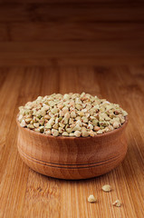 Green buckwheat in wooden bowl on brown bamboo board, close up. Rustic style, healthy dietary groats  background.