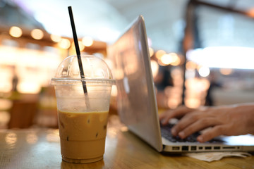 A half cup of coffee with soft light 2 hands typing on laptop. 2 man hands working on computer in coffee shop with a half cup of ice coffee on wooden table in airport with soft light bokeh background