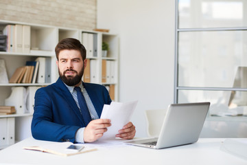 Fototapeta na wymiar Portrait of successful bearded businessman looking away pensively while working at desk in modern office