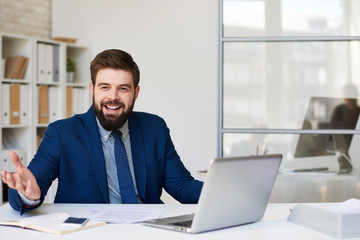 Fototapeta na wymiar Portrait of successful bearded businessman smiling happily while working at desk i9n modern office