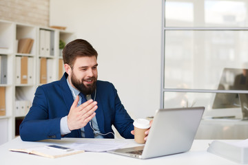 Portrait of smiling bearded businessman speaking with partner via laptop by video chat meeting