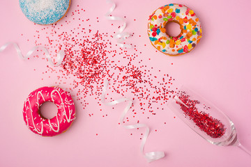 Flat lay of Celebration. champagne glass with colorful party streamers and delicious donuts on pink...
