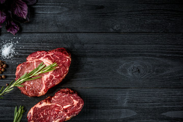 Fresh raw beef with basil and a sprig of rosemary on black wooden background