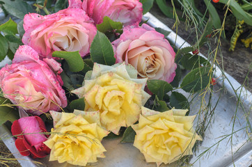 a bouquet of yellow pink and red roses lies on an old metal tray