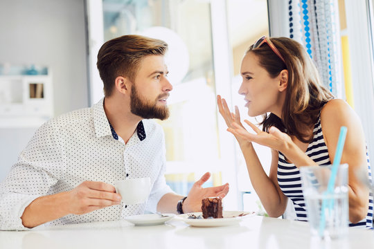 young couple arguing while sitting and drinking coffee in restaurant