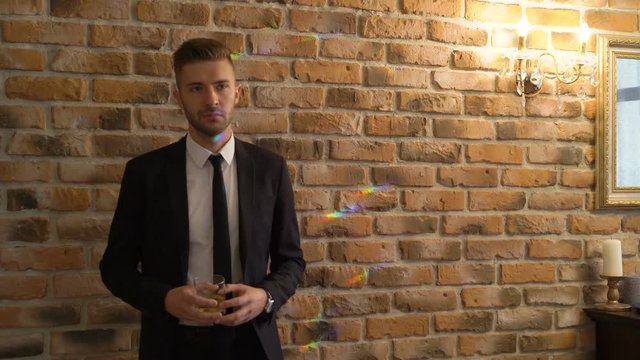 Man in a suit with glass of whiskey seduces girl. Beautiful blonde young sexy woman greets, kisses, hugs a guy close to brick wall