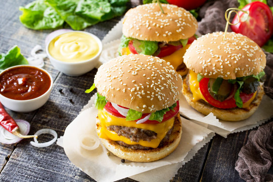 A double burger with a meat cutlet and vegetables is served with cheese sauce and ketchup. Delicious fresh homemade double cheeseburger on a wooden kitchen table. Street food, fast food.
