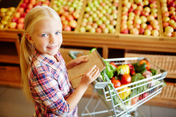 Cute girl making list of goods to buy in supermarket