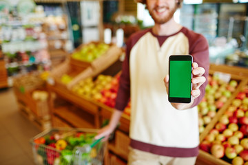 Obraz premium Young buyer showing promo advert in his smartphone while visiting supermarket
