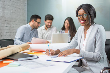 Portrait of young businesswoman taking notes on meeting with business partners and looking at camera in office.