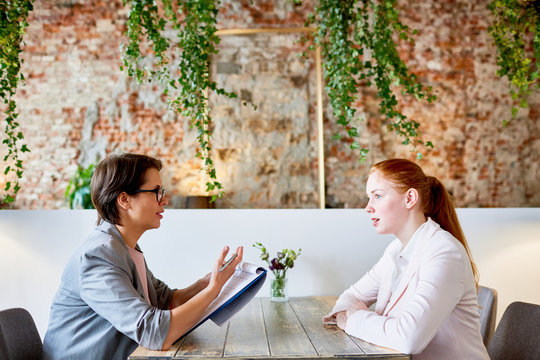 Young applicant answering questions of employer during appointment in cafe