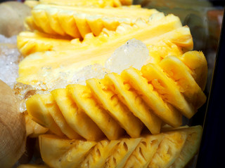 Peeled fresh yellow swirly cut pineapple pieces topped with ice in glass display cabinet of Thai local traditional fruit street stall shop cart