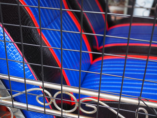 Blue, red, black stripe line pattern leather sofa back seat of Thai local traditional taxi car "Tuk Tuk" with black wire grille square net cage wall, and stainless steel fence foreground