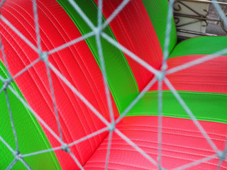 Close up of green red stripe pattern leather back seat of open air Thai local taxi car "Tuk Tuk" with triangle detail rope net as wall fence foreground