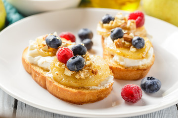 Crostini with ricotta cheese, fried pear, nuts and honey, decorated with raspberries and blueberries