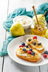 Crostini with ricotta cheese, fried pear, nuts and honey, decorated with raspberries and blueberries