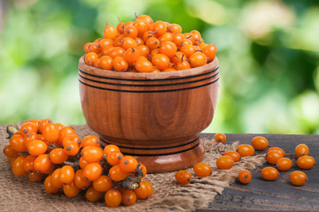 Sea-buckthorn berries in a wooden bowl on table with blurred garden background