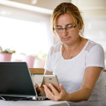 Middle-aged woman using laptop and phone at home 
