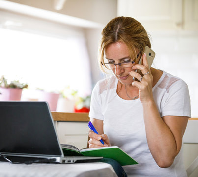 Middle-aged woman using phone and laptop at home 