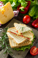 Pressed and toasted double sandwich with fresh vegetables and cheese, served with lettuce leaves on a cutting board.