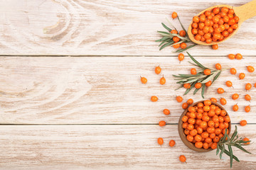 Sea buckthorn. Ripe fresh berries in bowl on white wooden background with copy space for your text. Top view