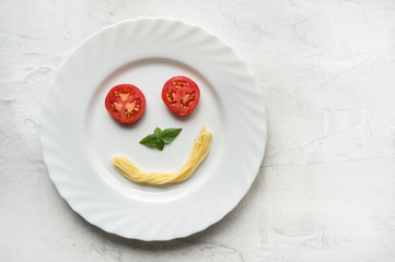 Smile face made from tomato, pasta and green basil leaf. Top view food photo. 