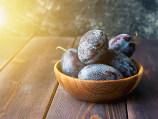 Fresh ripe plums in wooden bowl at sunlight