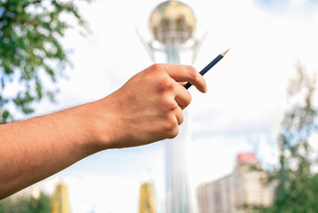 Pencil on the hands, background Astana. The hand of the creative artist.