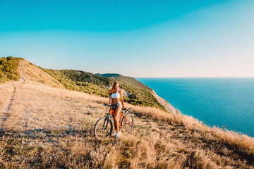 Fototapeta premium Beautiful woman on red mountain bicycle in the mountains and background of sea