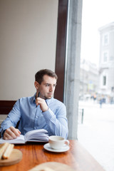 Young man looking attentively through window while sitting in cafe