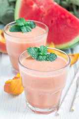Watermelon, peach, mint and coconut milk smoothie in glass on white wooden background, vertical