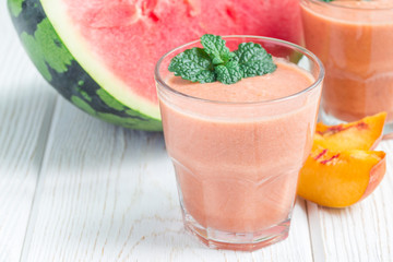 Watermelon, peach, mint and coconut milk smoothie in glass on white wooden background, horizontal, copy space