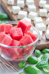 Ingredients for watermelon salad or caprese. Watermelon, feta and basil on wooden cutting board and in glass, vertical