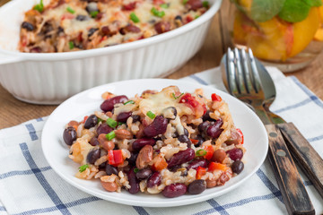 Baked casserole with different kinds of beans, rice and cheese, on a white plate and in ceramic baking dish, horizontal