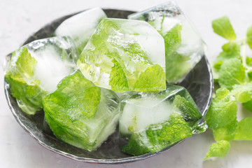 Homemade ice cubes with mint leaves inside on metal plate, fresh mint on background, ice for lemonade and cocktail, horizontal