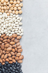 Different kinds of beans: black, pinto, white, chickpeas, on concrete background, copy space, vertical
