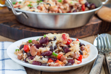 Baked casserole with different kinds of beans, rice and cheese, on a white plate and in metal baking dish, horizontal