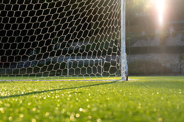 Football ground, evening sun backlit, goalpost and net in foreground