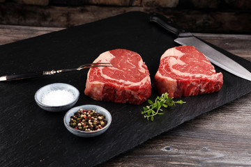 Raw fresh meat Ribeye Steak, seasoning and meat fork on dark background
