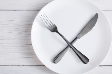 Empty plate with crossed fork and knife on white wood top view