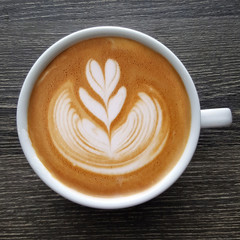 Top view of a mug of latte art coffee on timber background.