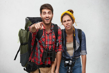 Excited male hitch hiker pointing with fore finger into distance while showing his female companion...