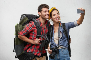 Family couple with backpacks taking selfie while posing against white background. Young energetic...